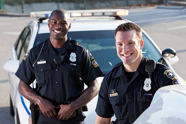 Multi-ethnic police officers (20s) standing in front of police car.